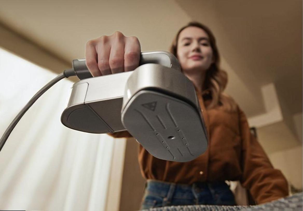 Kobieta trzyma ręczny parownicę nad deską do prasowania. Ujęcie z bliska.