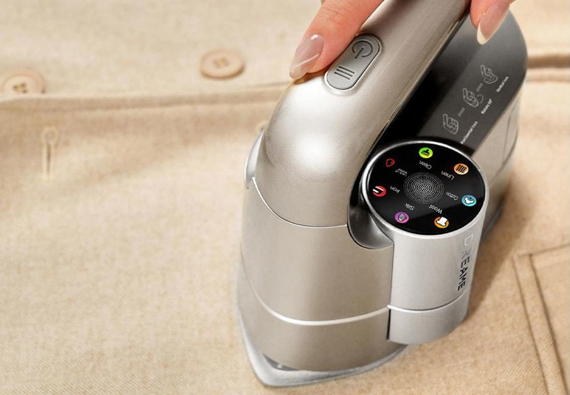 Dłoń trzyma żelazko na beżowym ubraniu z guzikami.