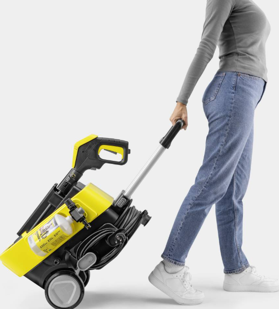 Osoba ciągnie za sobą żółtą myjkę ciśnieniową na kółkach.