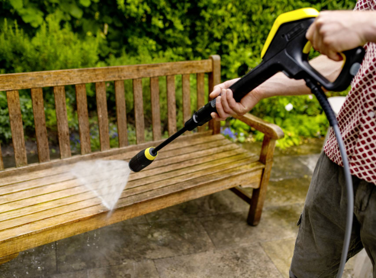 Osoba czyści drewnianą ławkę myjką ciśnieniową w ogrodzie.