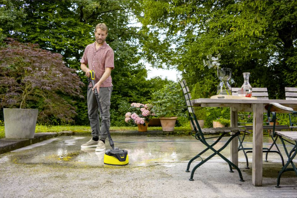 Mężczyzna czyści taras myjką ciśnieniową, meble ogrodowe w tle.
