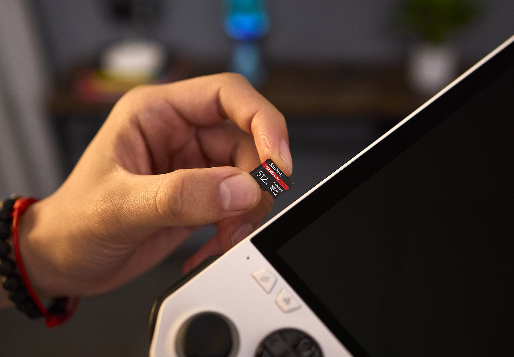 Une main tient une petite carte mémoire SanDisk 512 Go au-dessus d'un appareil portable blanc et noir.