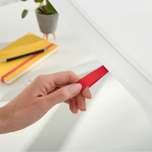 Eine Hand zieht ein rotes Band aus einer weißen Schublade. Ein Notizbuch liegt daneben.