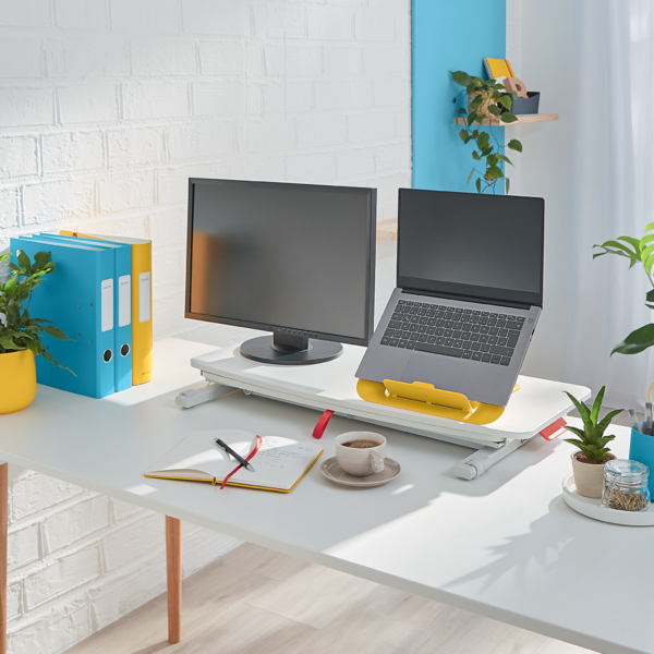 Ein Schreibtisch mit Laptop, Monitor, Notizbuch und Kaffeetasse.