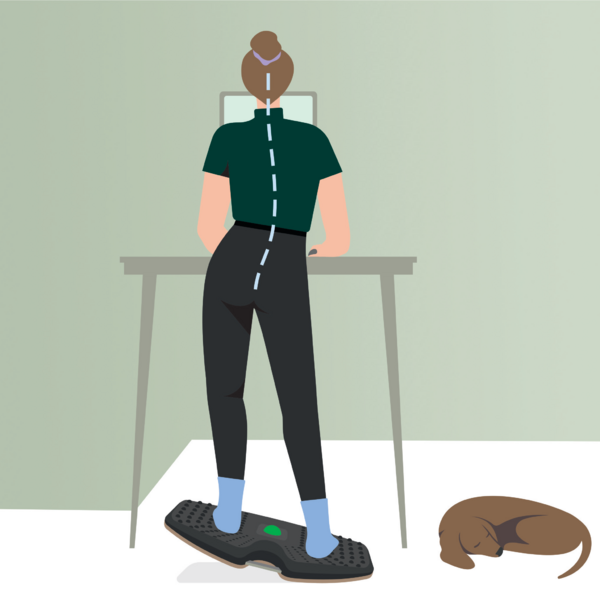 Eine Frau steht an einem Schreibtisch auf einem Balance Board, arbeitet am Laptop, mit einem schlafenden Hund in der Nähe.