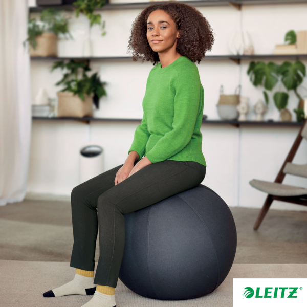 Eine Frau sitzt auf einem großen, grauen Gymnastikball vor einem Bücherregal.