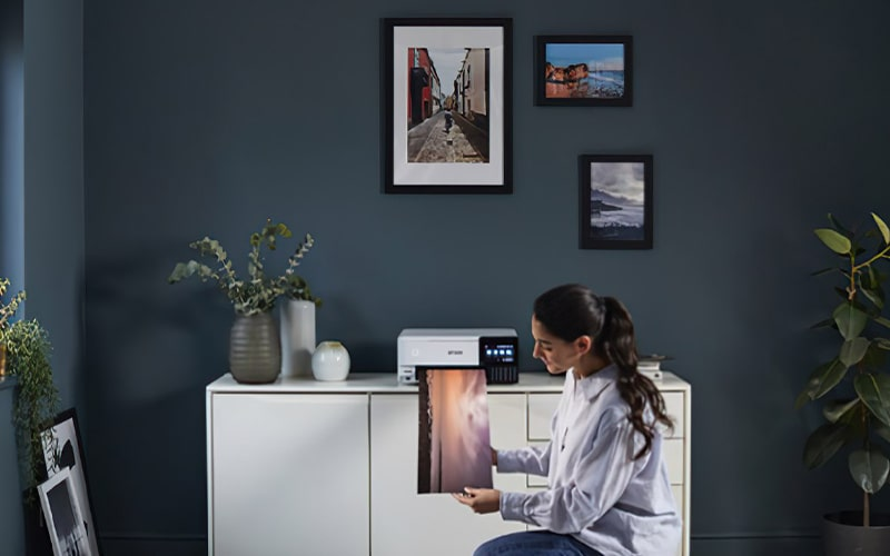 Kobieta trzyma wydrukowany obraz przed drukarką, wazony na szafce.