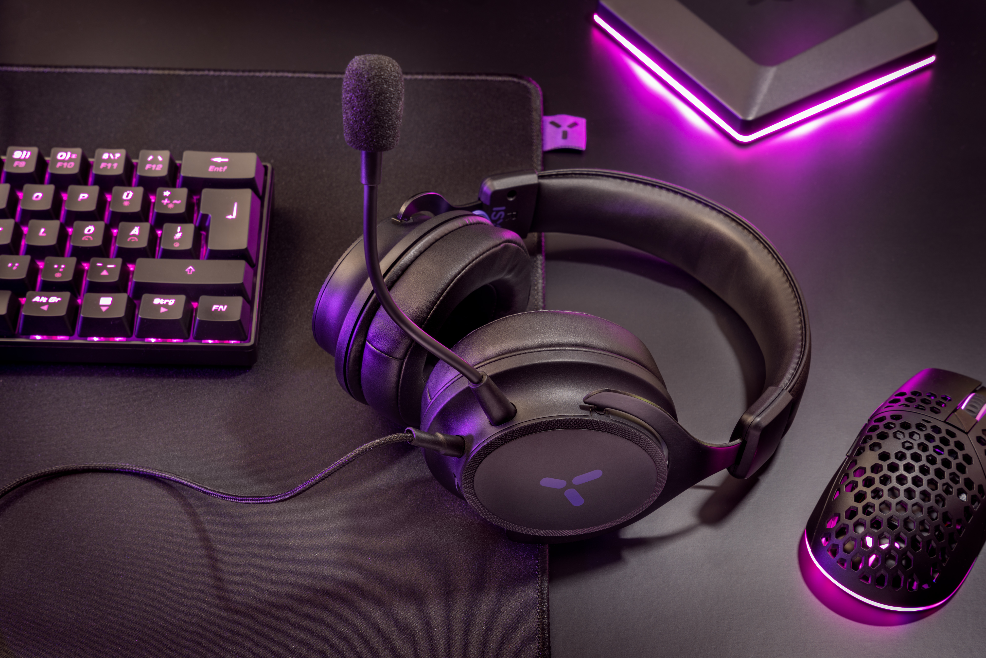 Czarne słuchawki gamingowe z mikrofonem, klawiaturą i myszką w fioletowym świetle.
