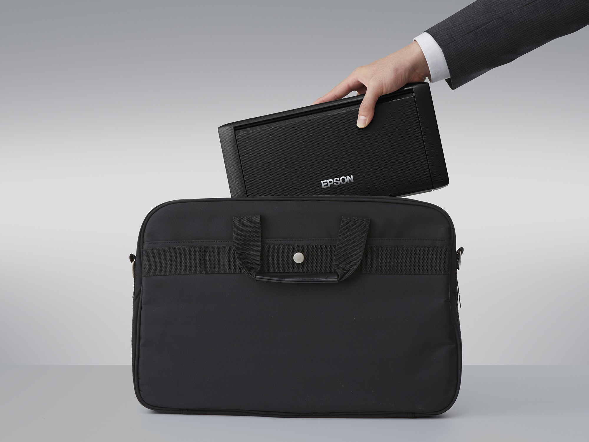 Ręka wkłada czarną drukarkę Epson do czarnej torby na laptopa.