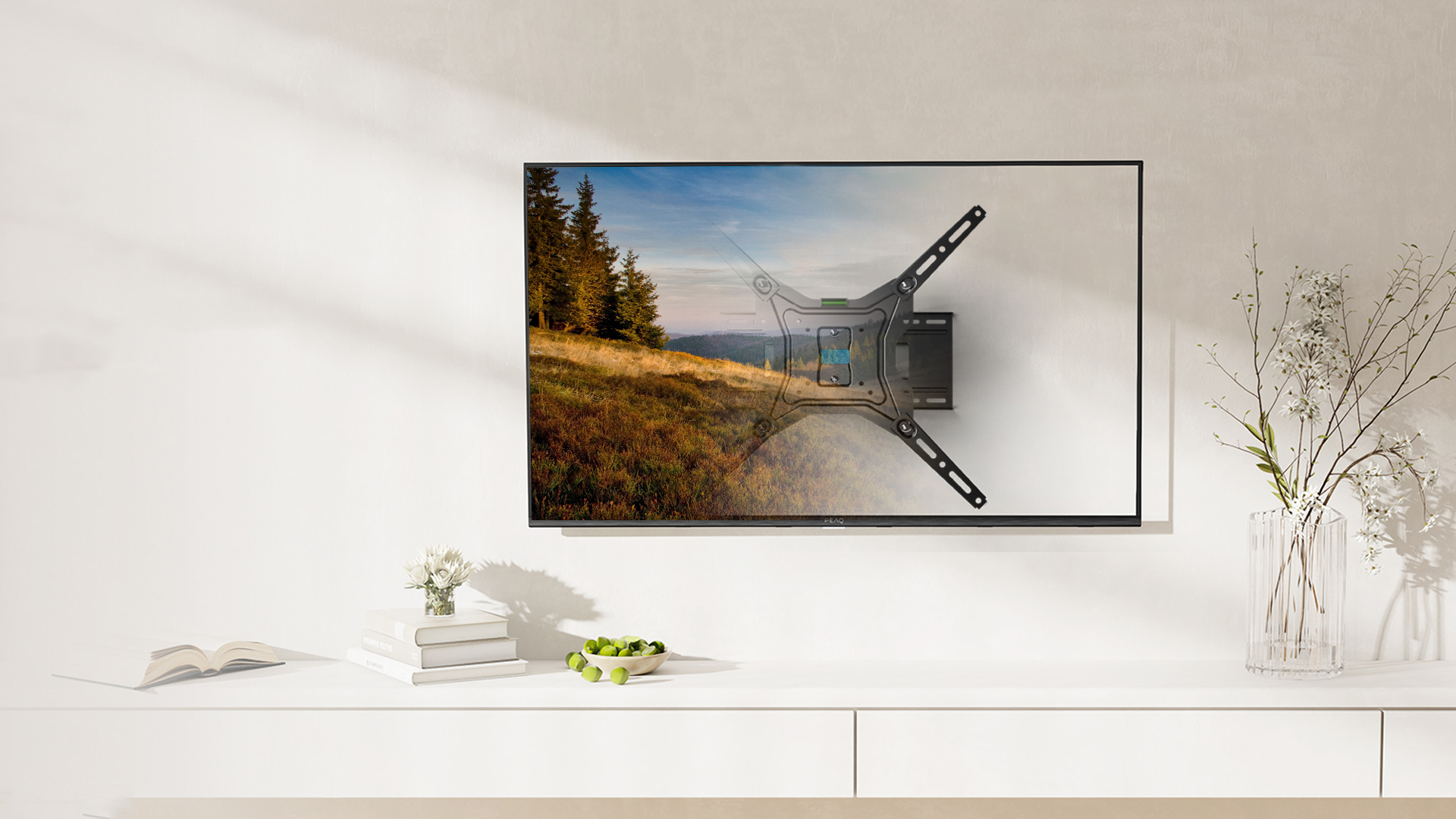 Telewizor na uchwycie ściennym pokazuje krajobraz. Na półce leżą książki i owoce.