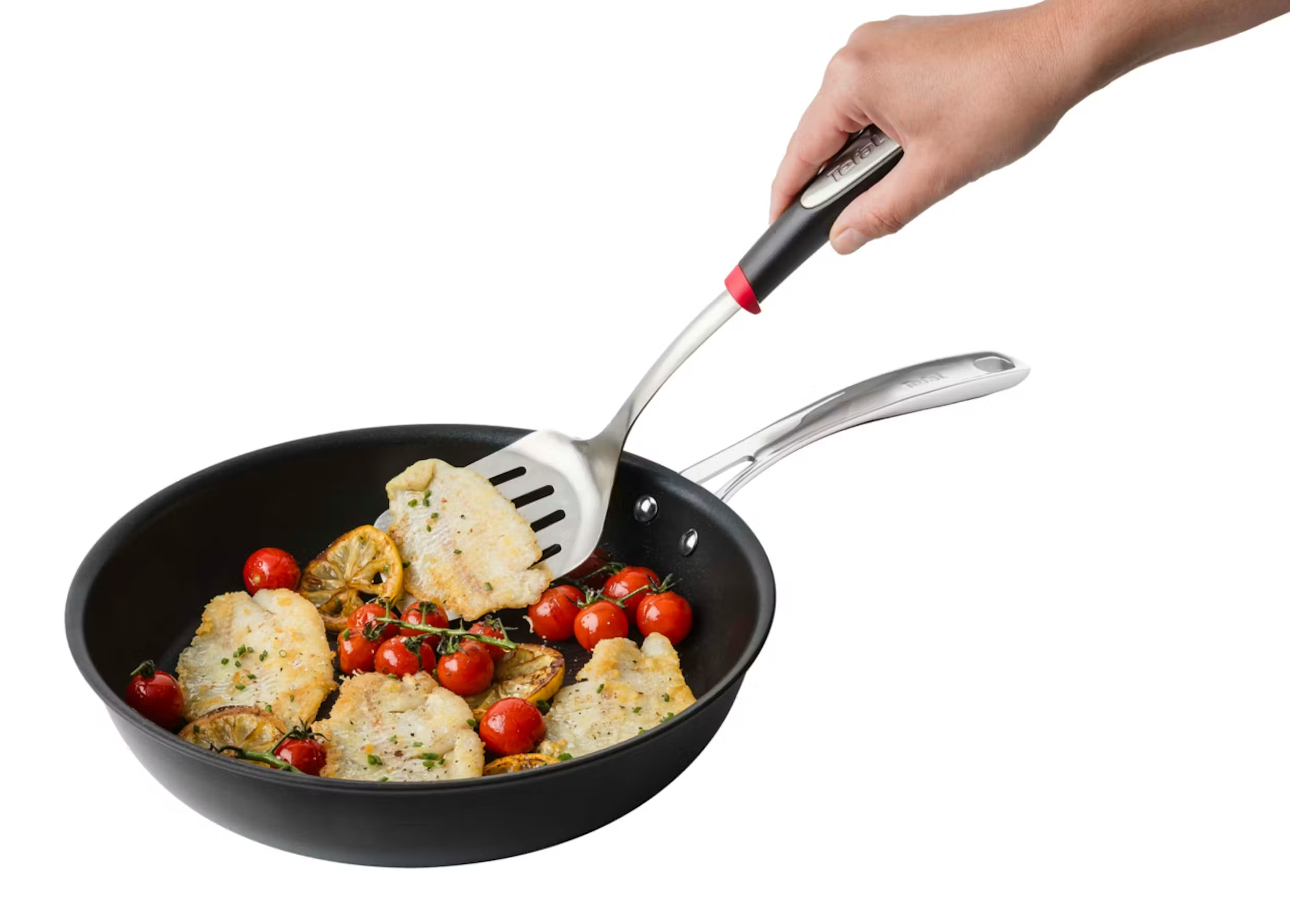 Łopatka podnosi kawałek smażonej ryby z patelni z pomidorkami koktajlowymi i cytryną.