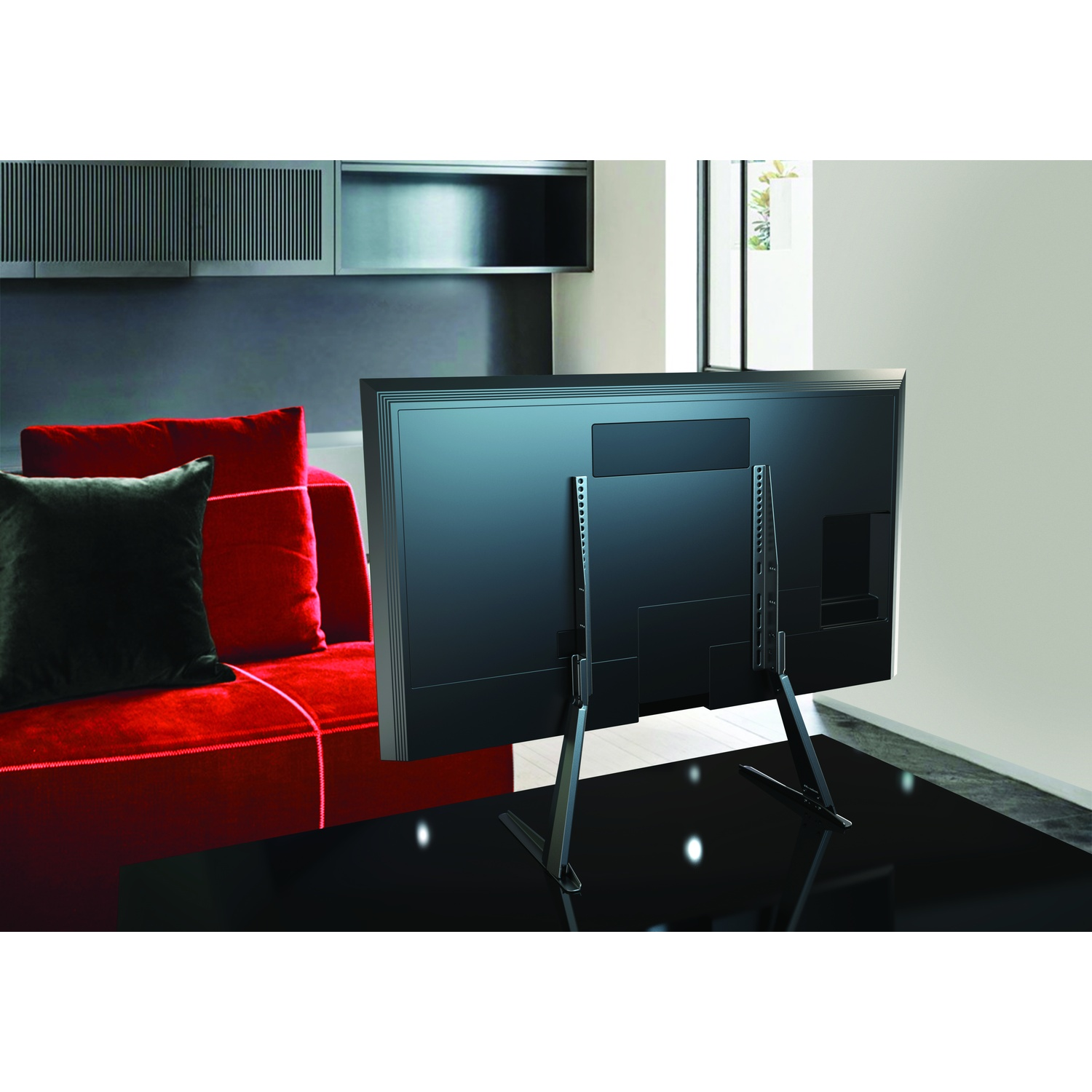 Retro di una TV su un supporto, con divano rosso e cuscini a sinistra.