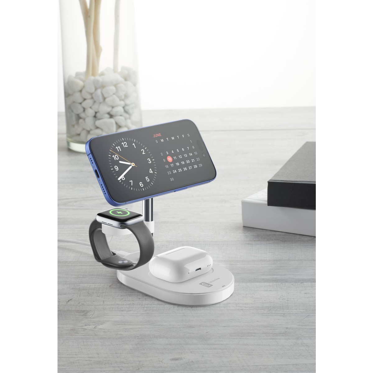 Un soporte de carga blanco sostiene un reloj inteligente y auriculares. Un teléfono muestra un calendario.