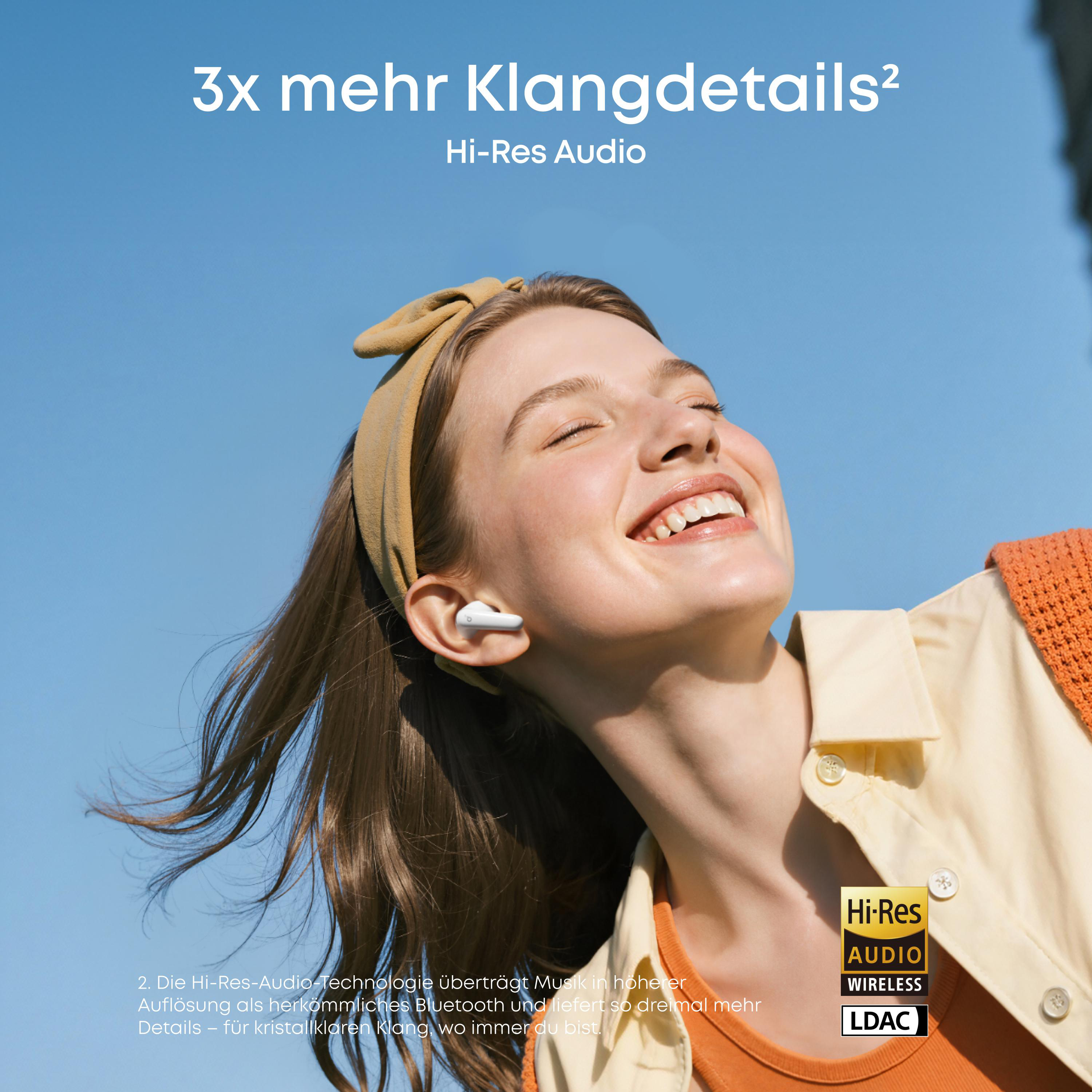 Frau mit Kopfhörern lacht gegen blauen Himmel. Hi-Res Audio.
