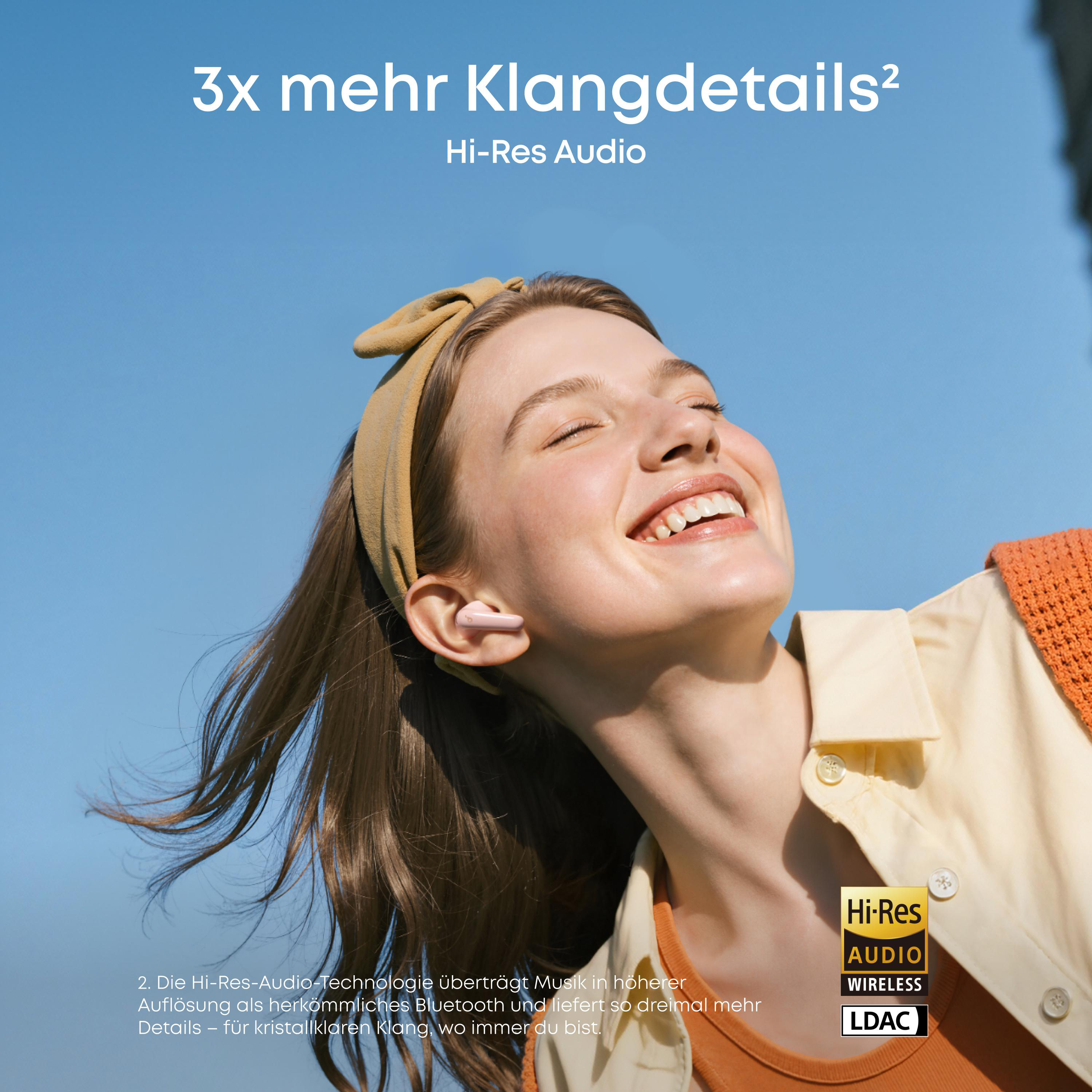 Junge Frau mit Kopfhörern lacht im Freien. "3x mehr Klangdetails".