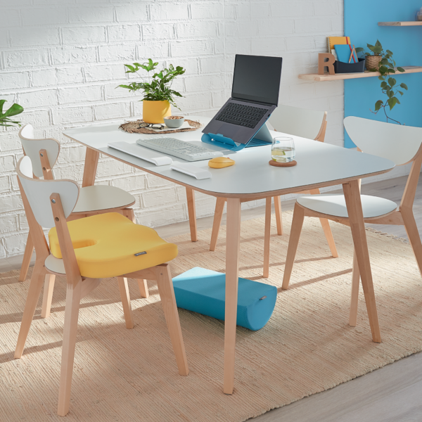Ein Schreibtisch mit Laptop, Tastatur, Maus, Kissen und Stühlen.