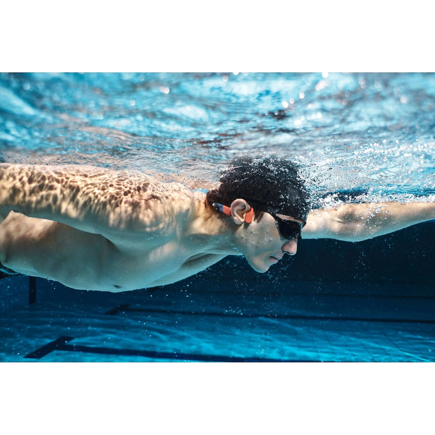 Un nageur portant lunettes et écouteurs nage sous l'eau dans une piscine.