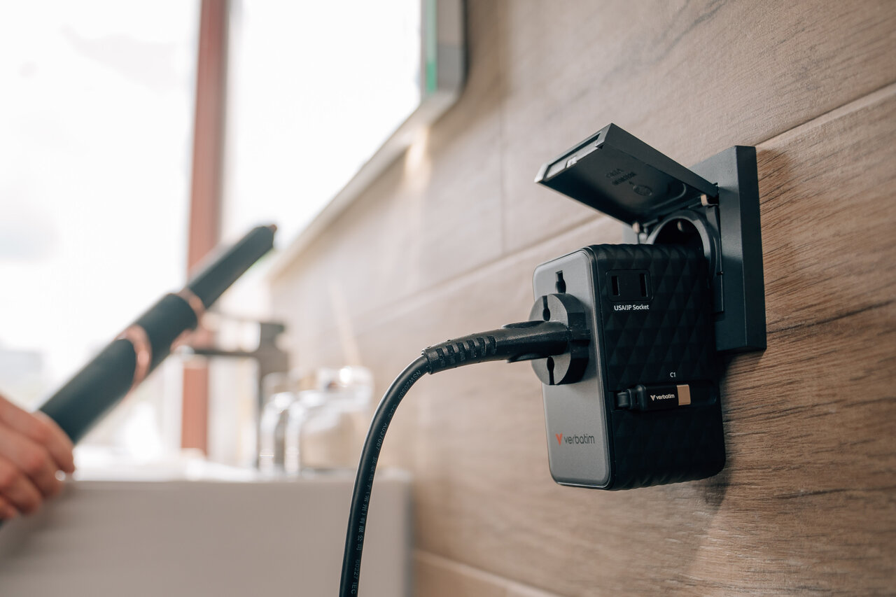 Egy utazási adapter van bedugva egy konnektorba egy fali falon.