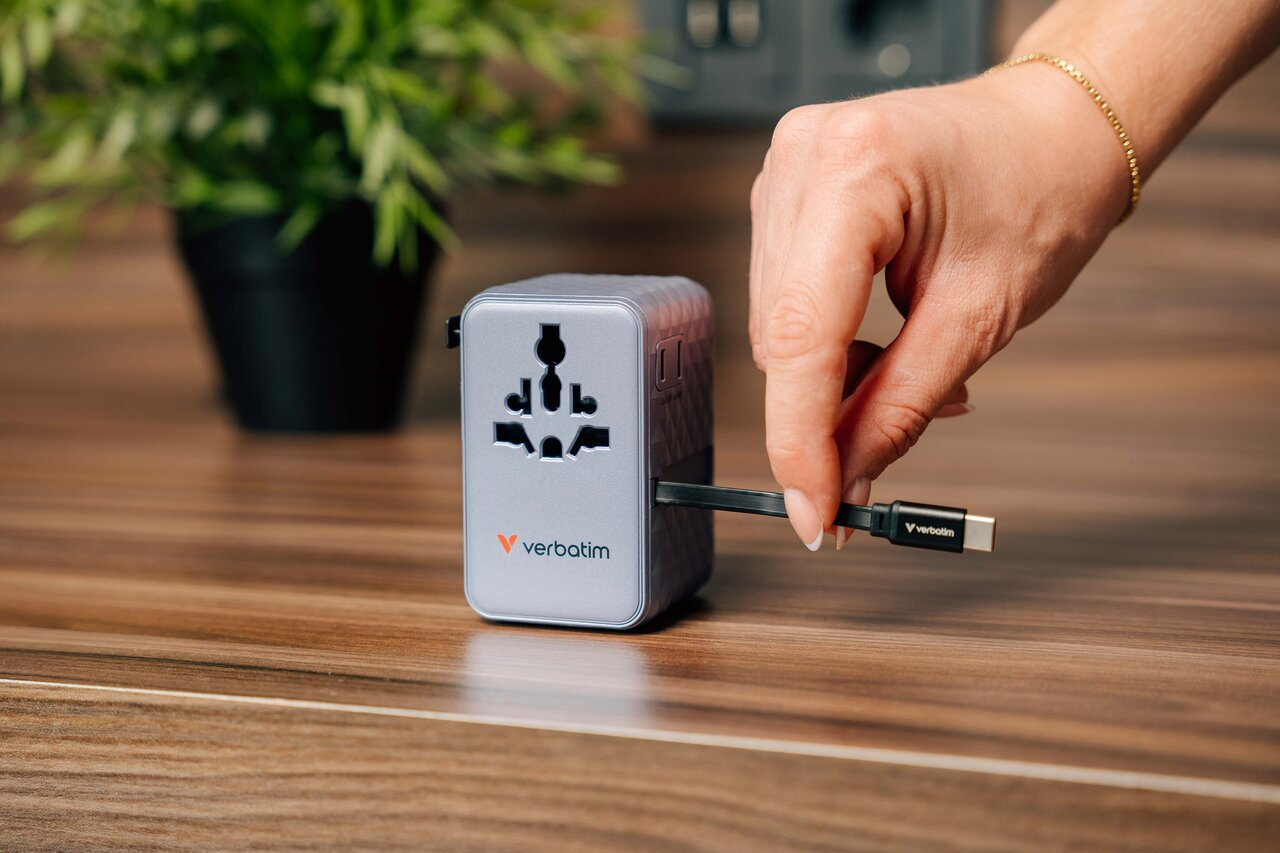 Egy kéz USB-C kábelt dug egy ezüst színű univerzális utazóadapterbe.