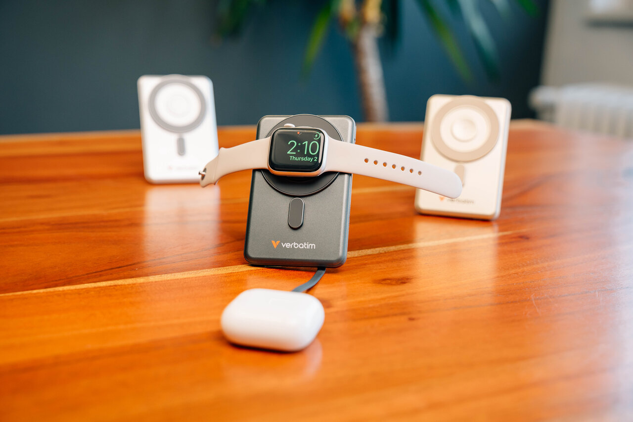 Szürke töltő Apple Watch-al és AirPods töltőtokkal fa asztalon.