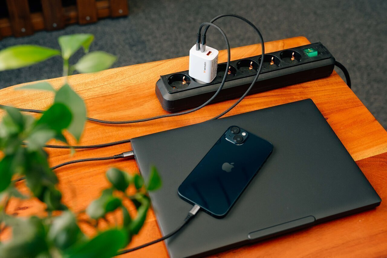 Laptop és iPhone töltődik egy elosztón egy faasztalon.