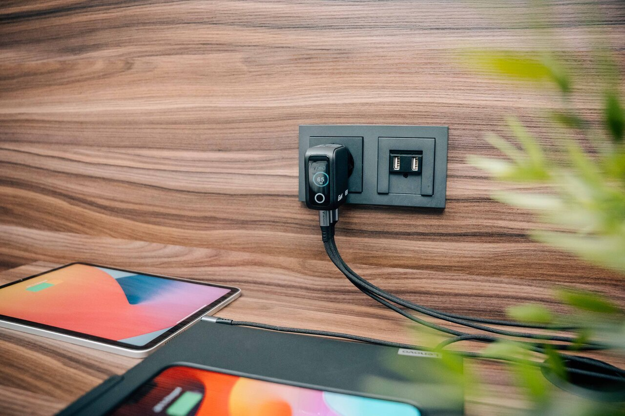 Egy töltő van bedugva egy USB-portokkal ellátott fali aljzatba. Több eszköz töltődik.