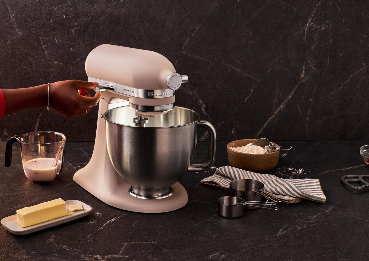 Ein beigefarbener Standmixer mit Metallschüssel, daneben Butter, Milch und Mehl.