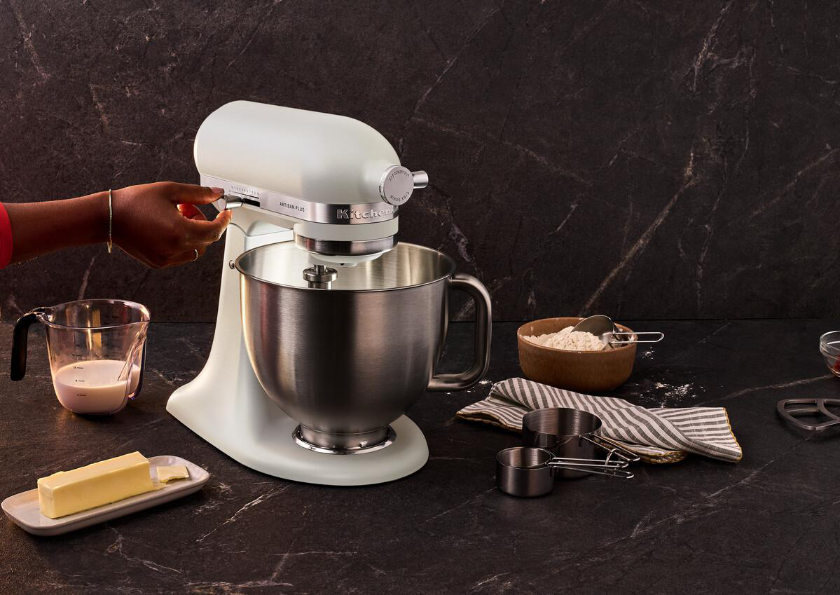 Eine cremefarbene KitchenAid-Küchenmaschine, deren Geschwindigkeit eine Hand einstellt. Zutaten in der Nähe.