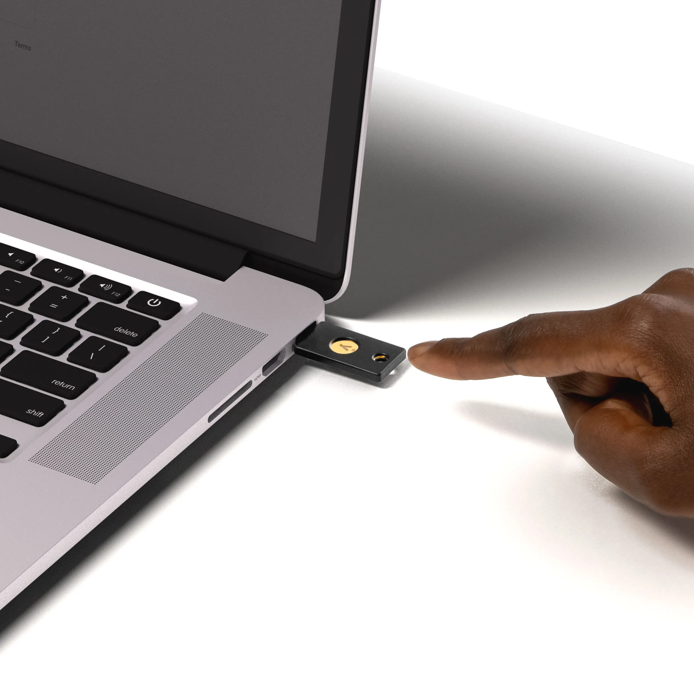 Ein Finger steckt einen USB-Schlüssel in einen Laptop, der auf einem weißen Tisch steht.