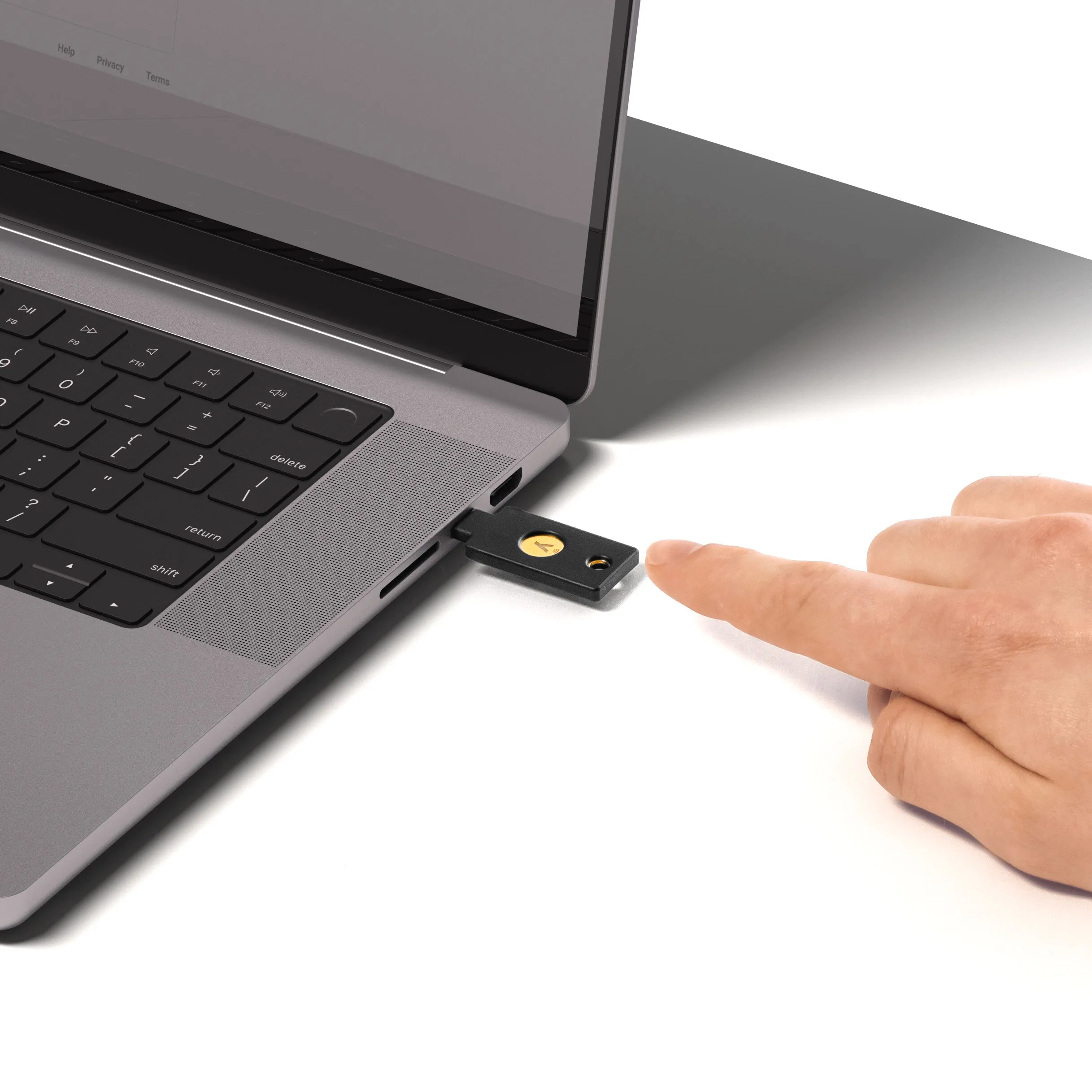 Ein Finger berührt einen schwarzen USB-Sicherheitsschlüssel, der in einen Laptop eingesteckt ist.