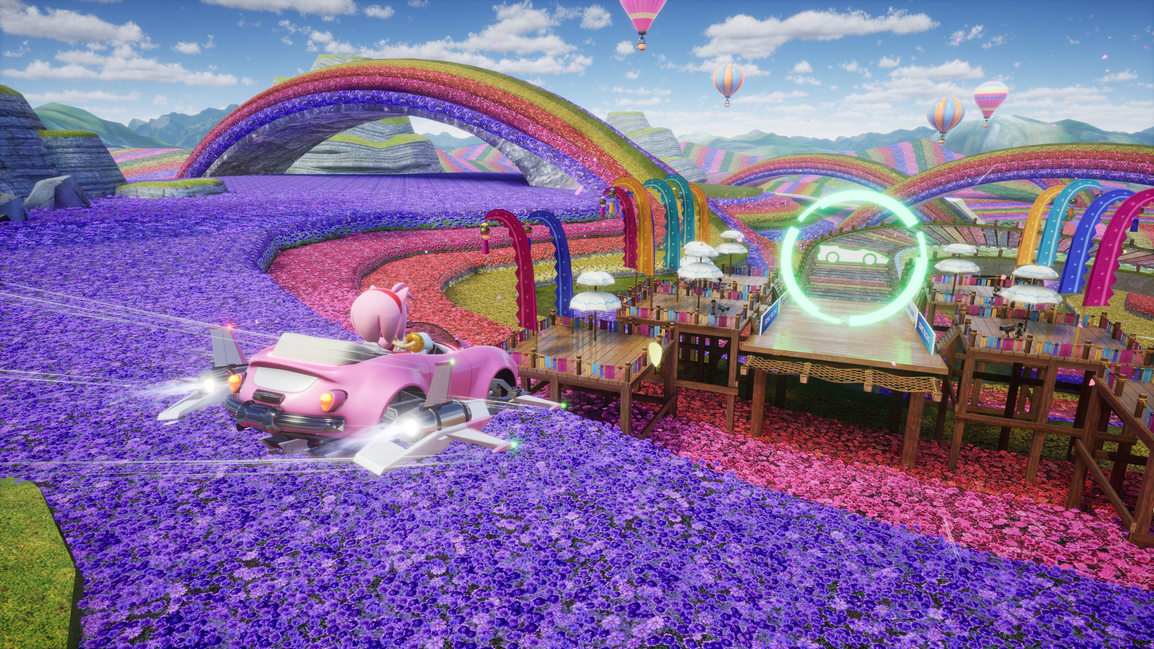 Un'auto rosa corre in un campo di fiori sotto un arcobaleno.