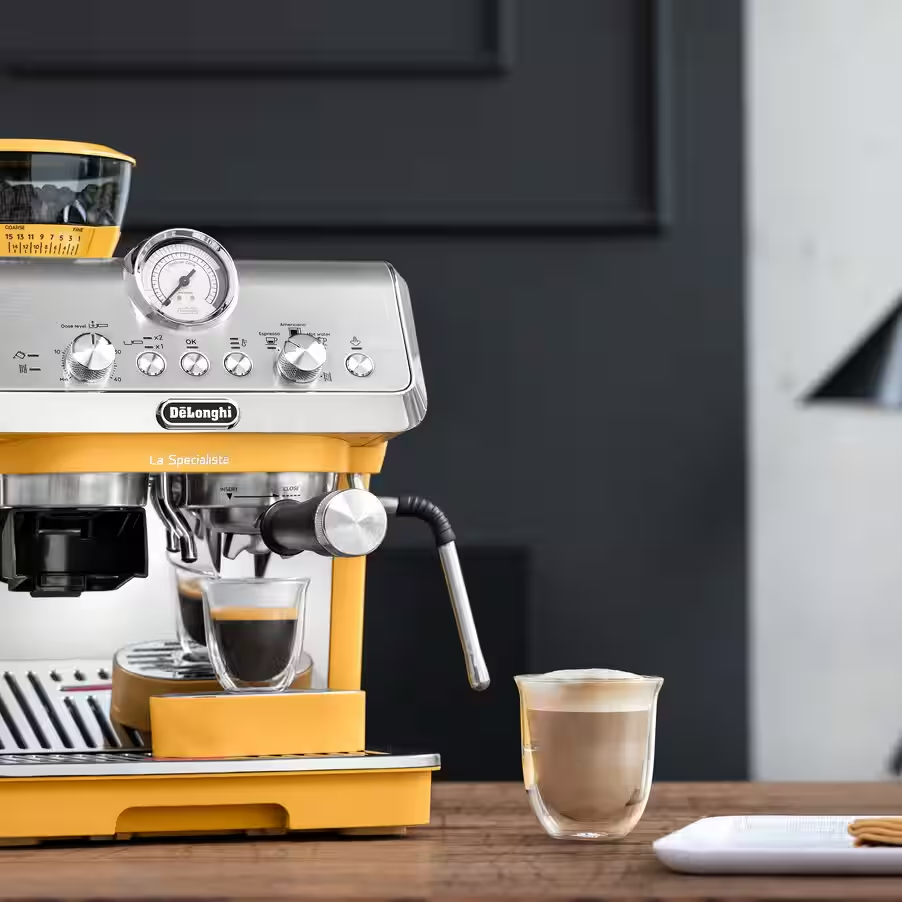 Egy sárga DeLonghi eszpresszógép két eszpresszóval és egy kapucsínóval.
