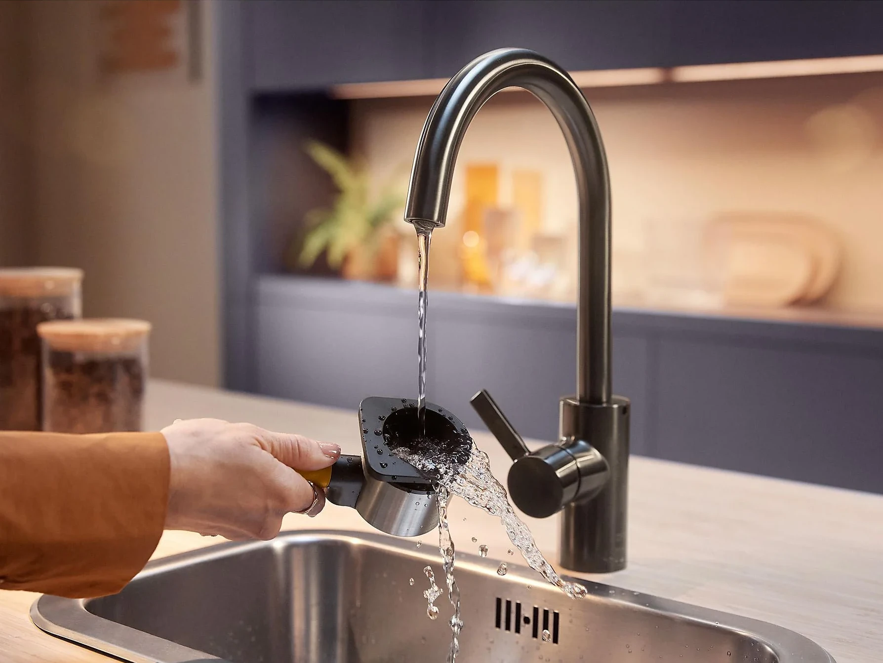 Ręka płucze część filtra do kawy pod bieżącą wodą z kranu w kuchni.
