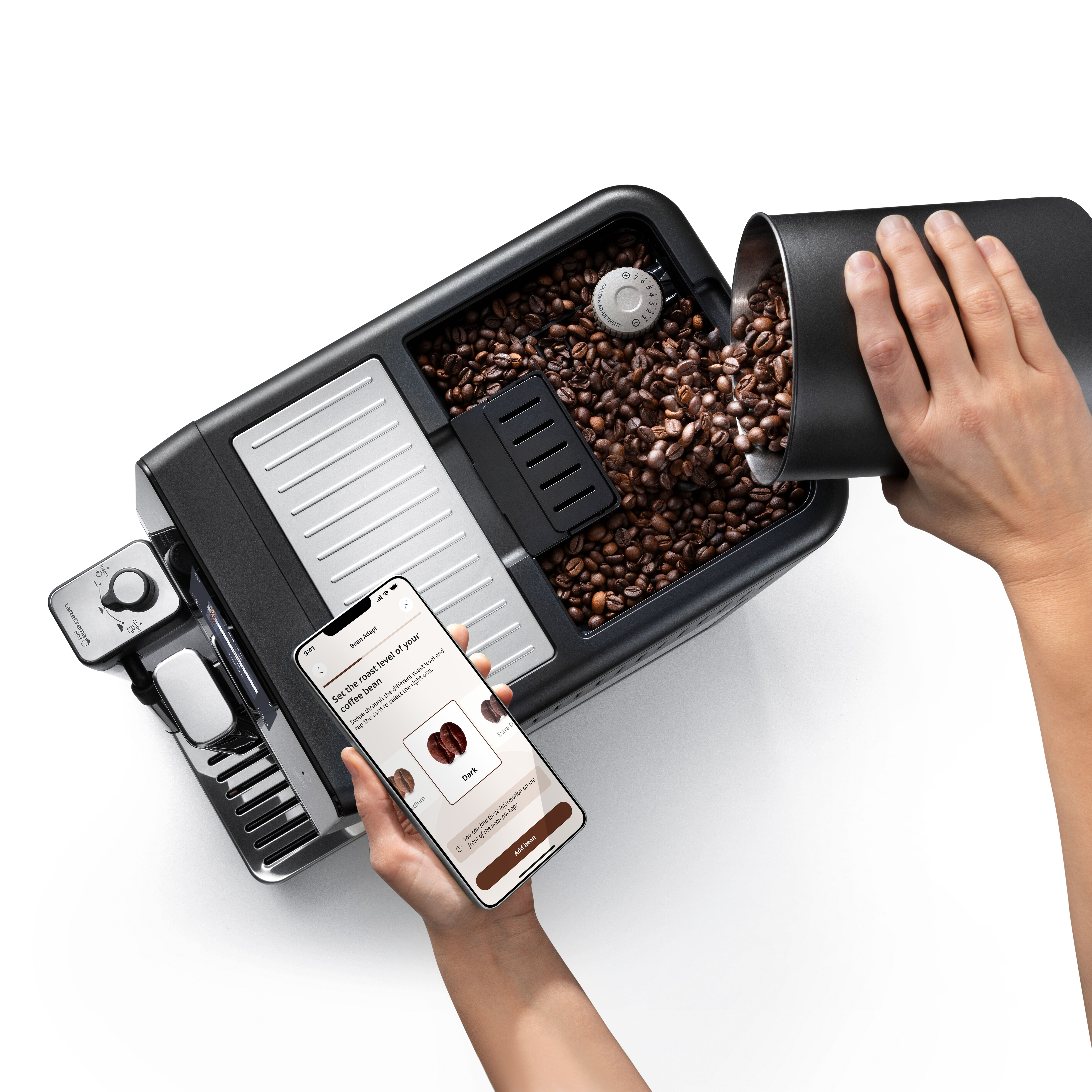 Eine Person füllt Kaffeebohnen in eine Kaffeemaschine, während sie ein Smartphone hält.