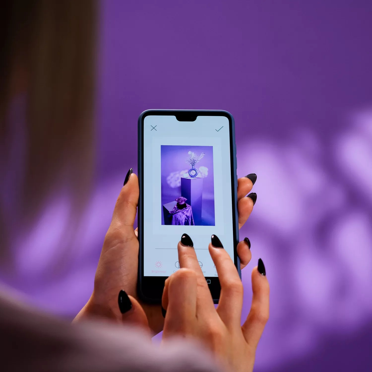 Dłonie z czarnymi paznokciami trzymają smartfon z fioletowym efektem edycji obrazu.