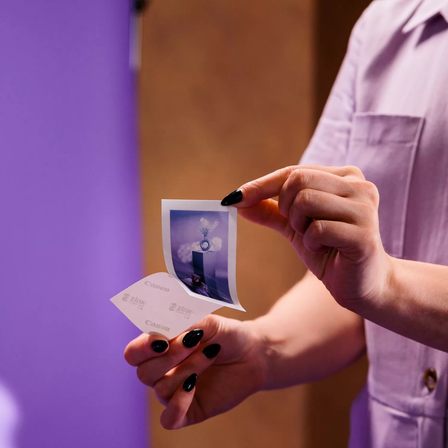 Osoba z czarnymi paznokciami trzyma małe zdjęcie z motywem wazonu.