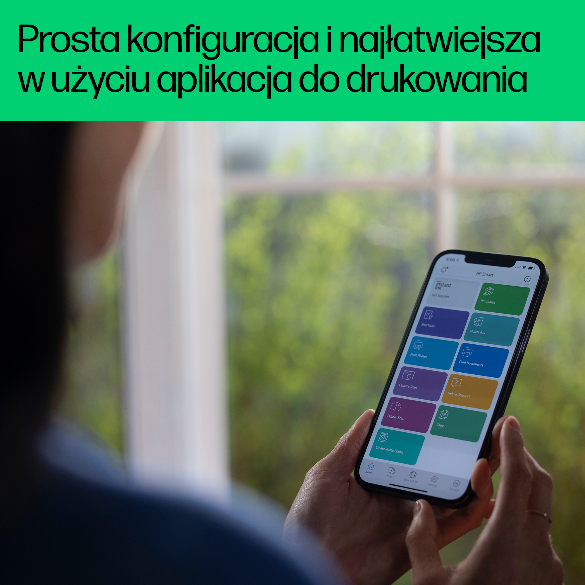 Osoba trzymająca smartfon z otwartą aplikacją HP Smart na jasnym tle.