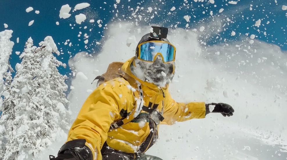 Snowboarder w żółtej kurtce jedzie przez śnieg, z kamerą GoPro na kasku.