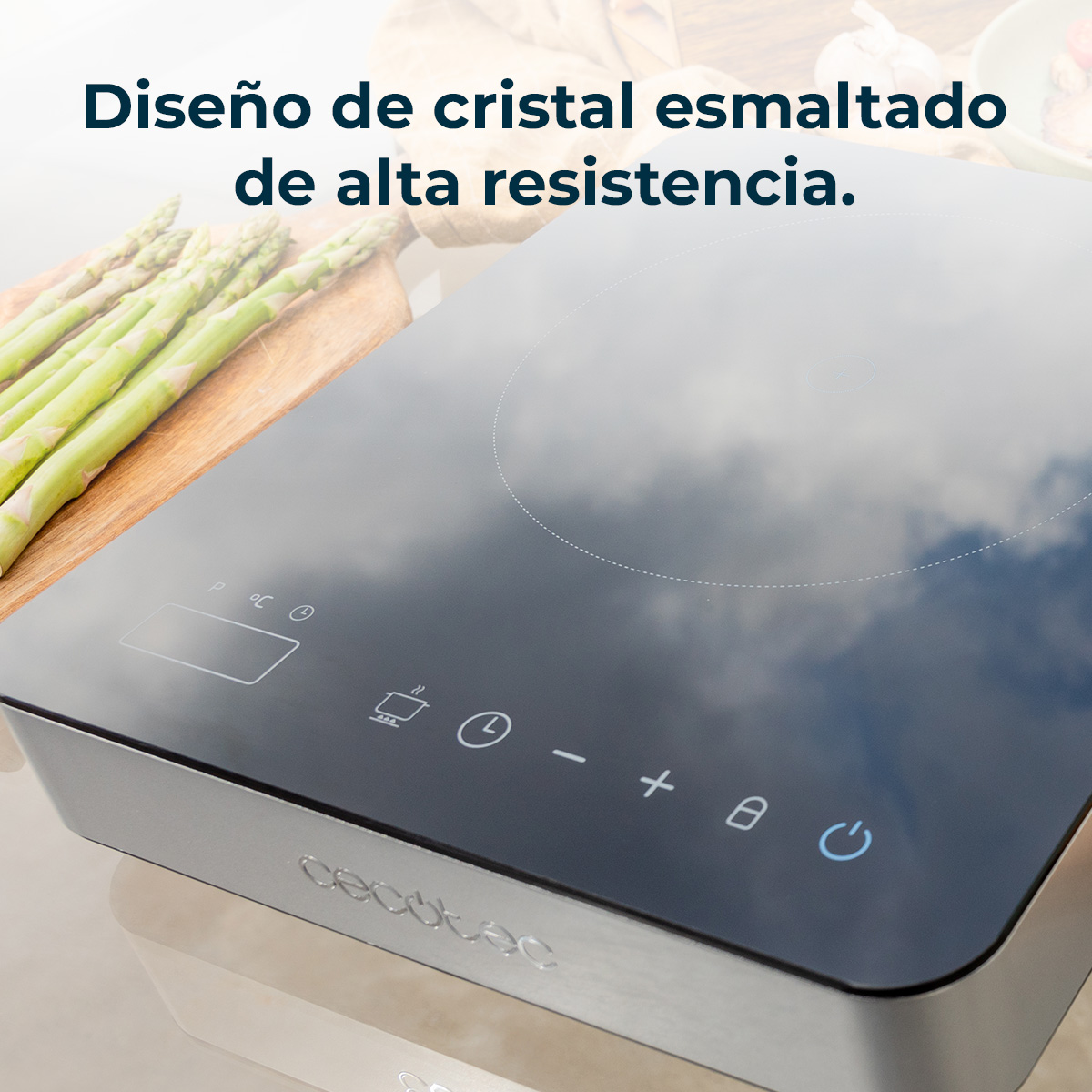 Placa de inducción con controles digitales y espárragos sobre tabla de madera.