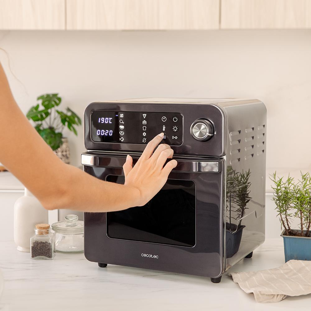 Una mano ajusta la hora en un horno freidora de aire oscuro.
