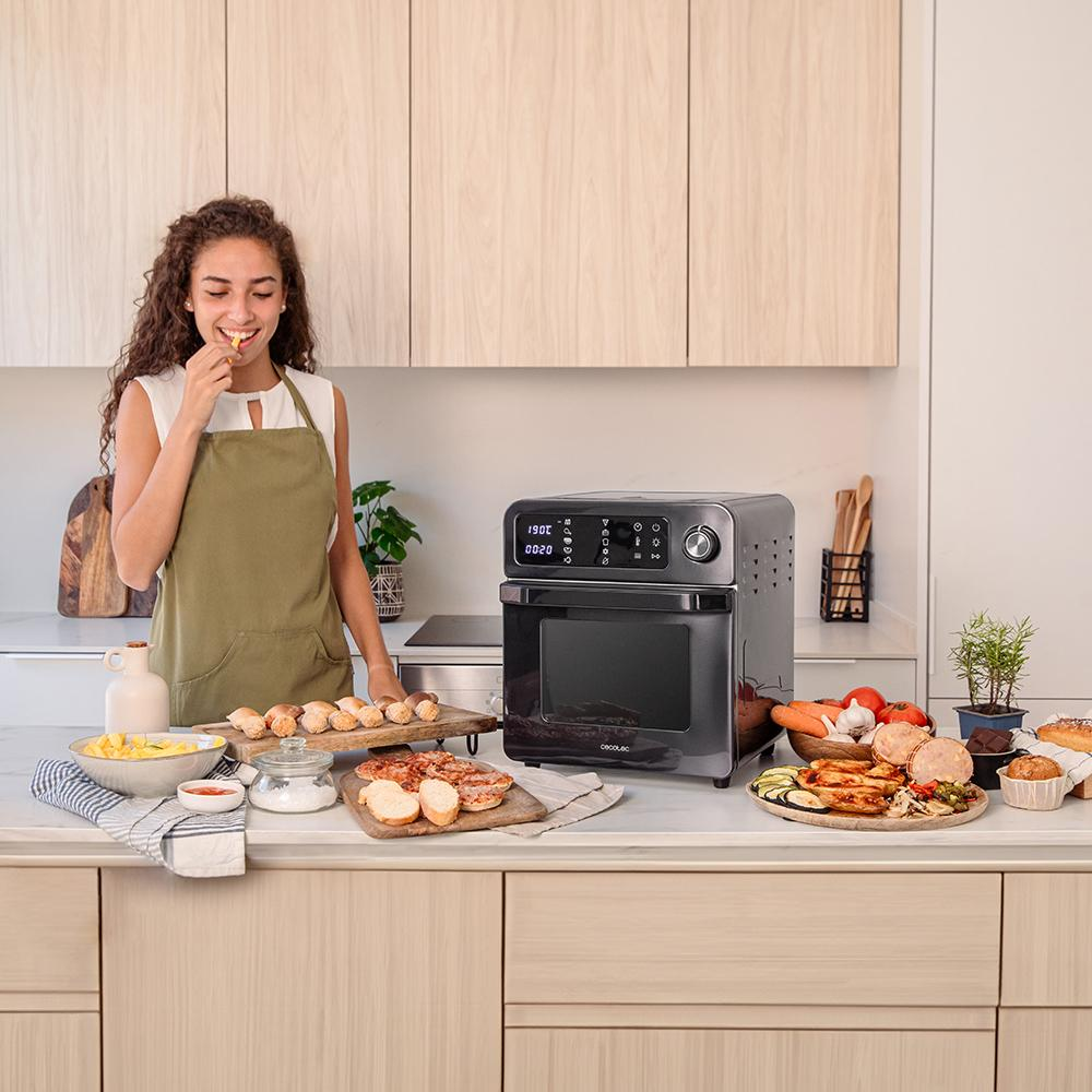 Una mujer come algo frente a una freidora de aire, rodeada de comida como patatas y carne.
