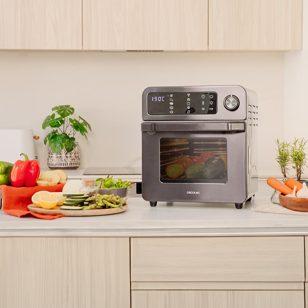 Un horno plateado moderno con verduras y limones en una encimera de cocina.