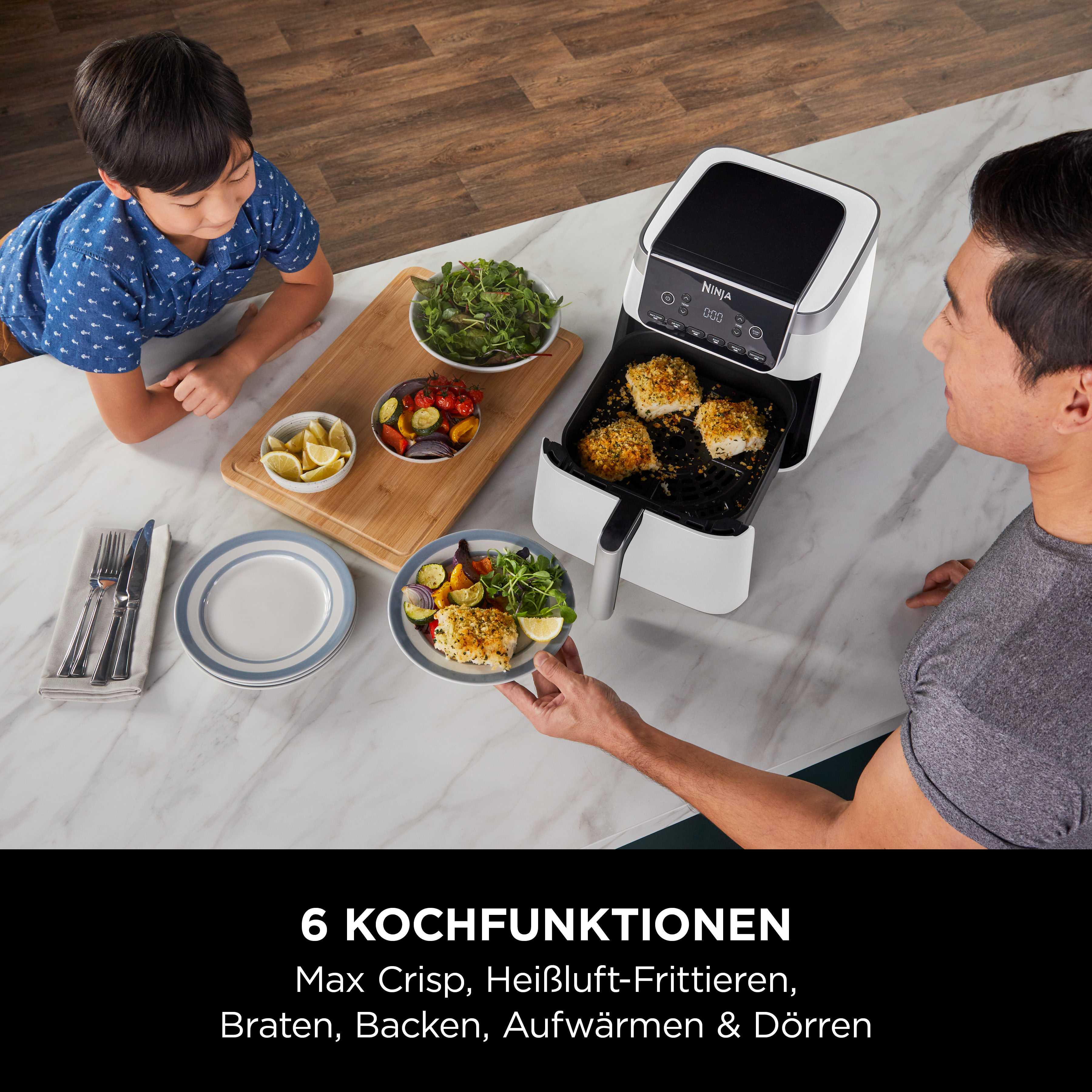 Un homme et un enfant à table avec une friteuse à air et des plats préparés.