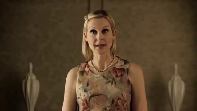 Eine Frau mit blonden Haaren trägt ein Blumenkleid und eine Perlenkette.