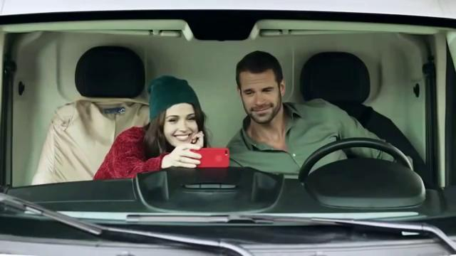 Frau und Mann im Auto, sie macht ein Selfie mit einem roten Handy.