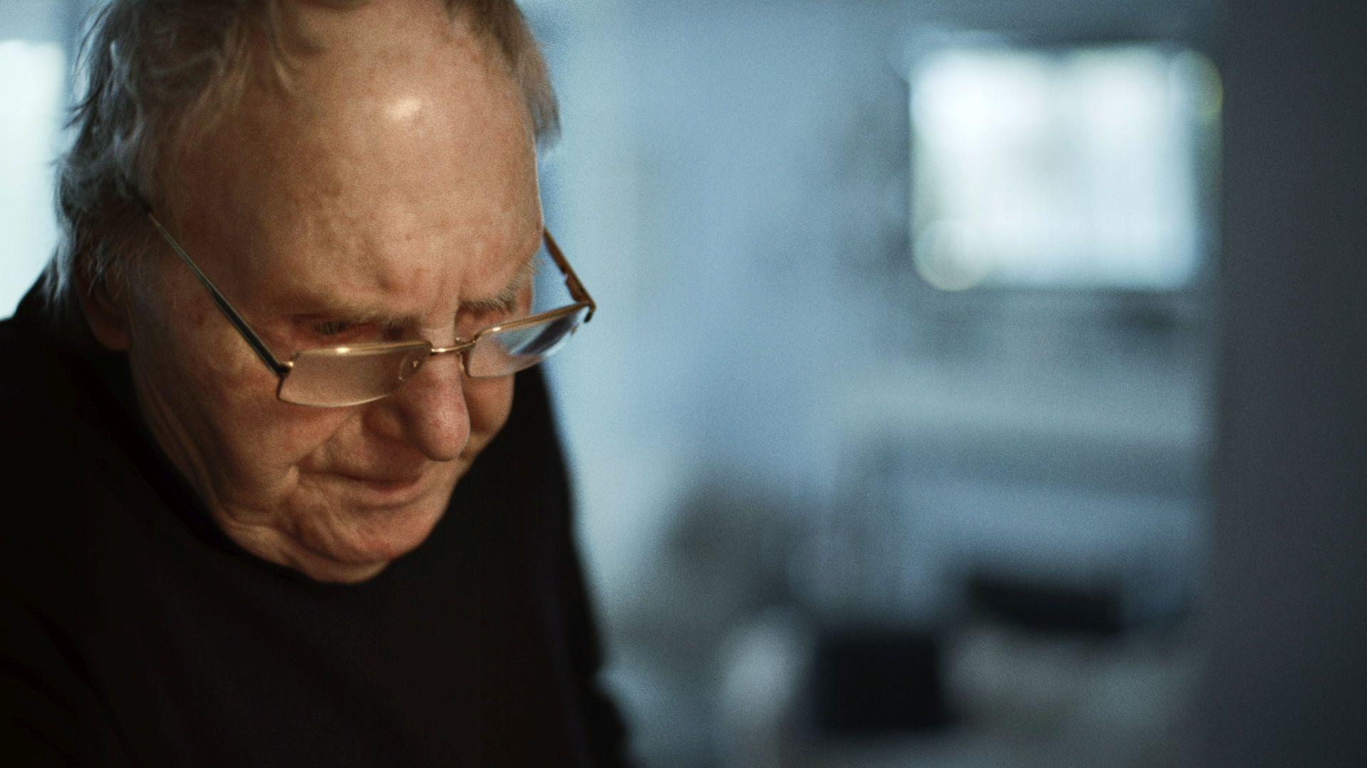 Ein älterer Mann mit Brille blickt nach unten. Sein Gesicht ist im Schatten.