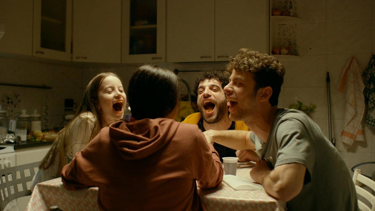 Vier Personen lachen am Esstisch in einer Küche. Orangefarbene Mündungen.