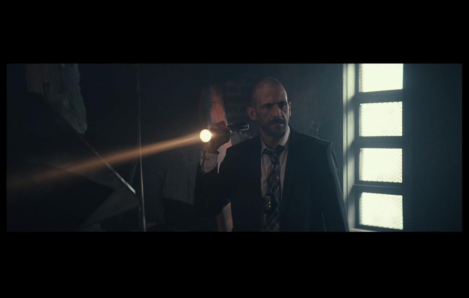 Ein Mann im Anzug leuchtet mit einer Taschenlampe in einem dunklen Raum.