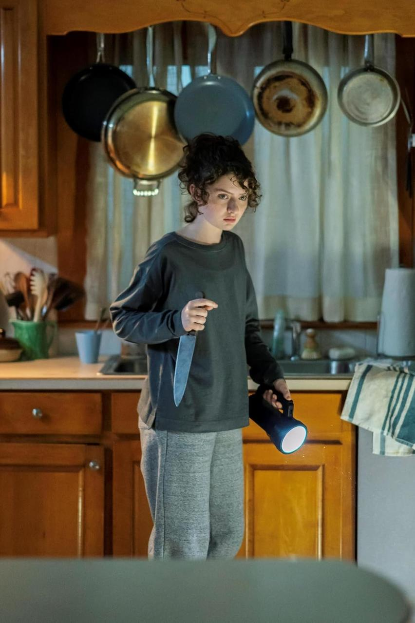 Ein Mädchen mit Locken hält ein Messer und eine Taschenlampe in einer Küche.