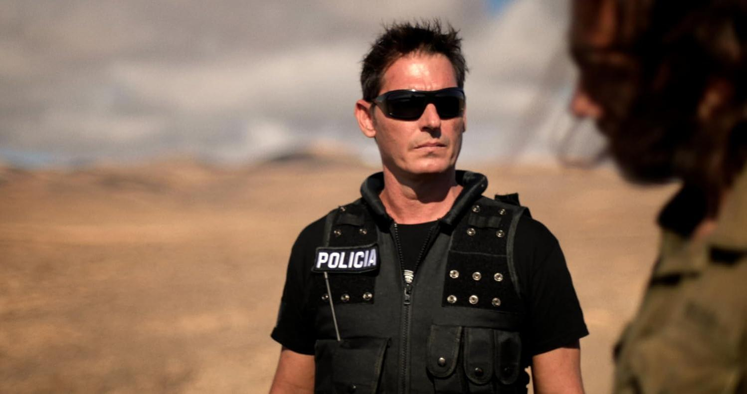 Ein Mann in Sonnenbrille und Polizeiweste steht im Freien.